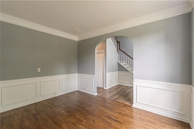 Unfurnished room featuring arched walkways, crown molding, wainscoting, wood finished floors, and stairway