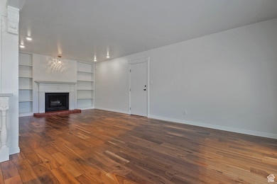 Unfurnished living room with built in shelves, a fireplace, dark wood-type flooring, and recessed lighting