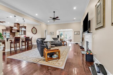 Living area with ceiling fan, arched walkways, a fireplace with raised hearth, dark wood-type flooring, and recessed lighting