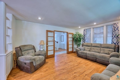 Living area with french doors, radiator heating unit, light wood finished floors, and recessed lighting