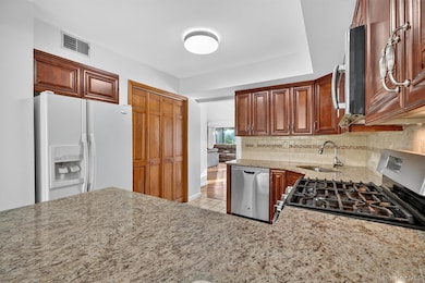 Kitchen with stainless steel appliances, tasteful backsplash, light stone countertops, brown cabinetry, and light tile patterned floors