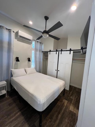 Bedroom with dark wood-style floors, a ceiling fan, recessed lighting, an AC wall unit, and a barn door