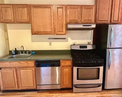 Kitchen with stainless steel appliances, dark countertops, under cabinet range hood, brown cabinets, and light wood-style flooring