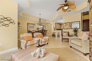 Living area with ceiling fan with notable chandelier, light tile patterned flooring, visible vents, a tray ceiling, and baseboards