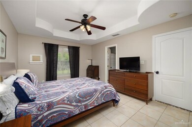 Bedroom with light tile patterned flooring, ceiling fan, and a tray ceiling