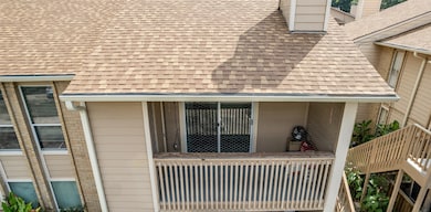 This photo shows a condo with a cozy balcony, featuring a sliding glass door and wood railing. The building has a shingled roof and beige siding, providing a warm, inviting exterior.