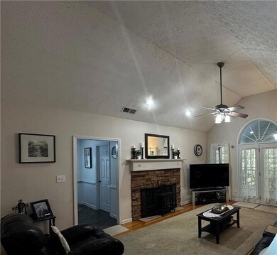 Living area featuring a textured ceiling, vaulted ceiling, wood finished floors, a ceiling fan, and a stone fireplace