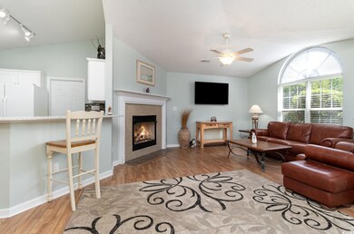 Living room with lofted ceiling, track lighting, ceiling fan, a tile fireplace, and wood finished floors