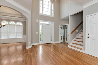 Entrance foyer with a chandelier, arched walkways, light wood-style floors, ornamental molding, and stairway