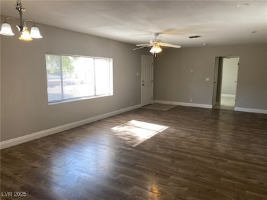 Empty room with a chandelier, ceiling fan, dark wo
