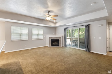 Open Living Area featuring ceiling fan, carpet flooring, a fireplace, a tray ceiling, and a textured ceiling