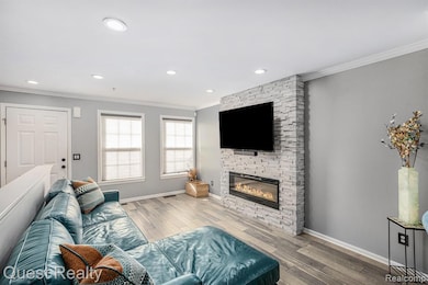 Living area featuring crown molding, wood-type flooring, a stone fireplace, and recessed lighting