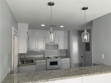 Kitchen featuring a textured wall, white range with electric stovetop, white cabinetry, tasteful backsplash, and decorative light fixtures
