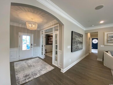 Foyer entrance featuring ornamental molding, a chandelier, dark wood-type flooring, and arched walkways