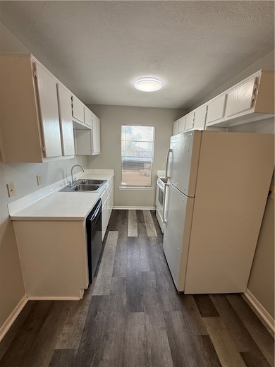 Kitchen with refrigerator, a textured ceiling, light countertops, dark wood-type flooring, and white cabinets