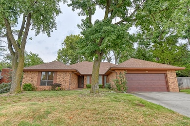 Single story home featuring a shingled roof, driveway, brick siding, and a front lawn