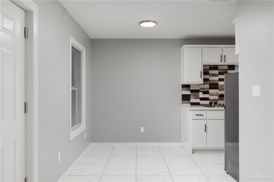 Kitchen featuring light marble finish flooring, white cabinetry, decorative backsplash, baseboards, and a sink