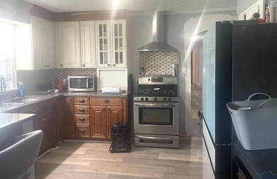 Kitchen featuring appliances with stainless steel finishes, wall chimney range hood, backsplash, and light wood-style floors