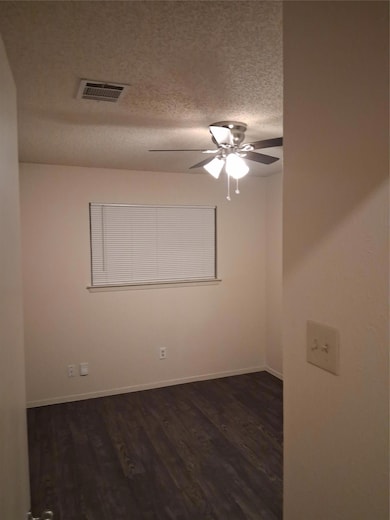 Unfurnished room featuring dark wood-type flooring, a textured ceiling, and a ceiling fan