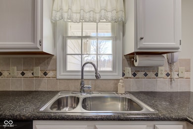 kitchen with decorative backsplash, white cabinets, dishwasher, and a sink