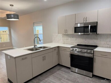 Kitchen featuring sink, kitchen peninsula, appliances with stainless steel finishes, hanging light fixtures, and dark wood-type flooring