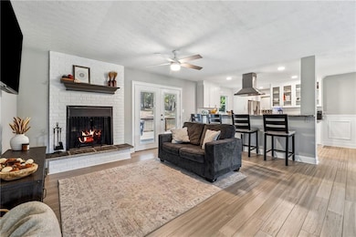 Living room with ceiling fan, a brick fireplace, light wood-type flooring, recessed lighting, and a textured ceiling