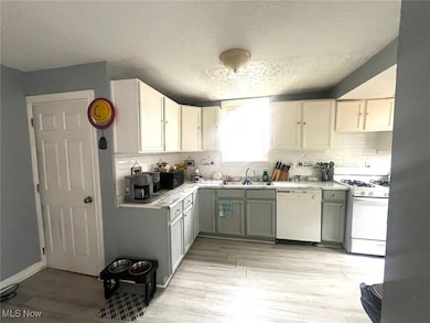 Kitchen featuring light countertops, a textured ceiling, light wood-type flooring, white appliances, and white cabinetry