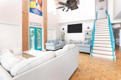 Living room with a towering ceiling, stairs, a ceiling fan, and french doors