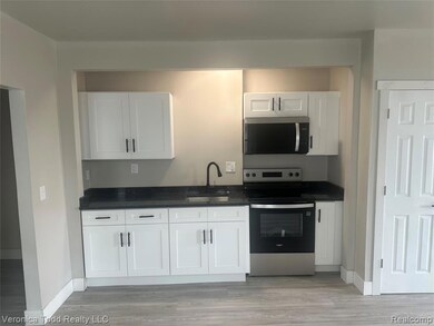 Kitchen with stainless steel appliances, white cabinetry, light wood finished floors, and dark stone countertops