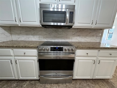 Kitchen featuring appliances with stainless steel finishes, white cabinetry, tasteful backsplash, and dark stone counters