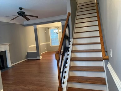 Stairway featuring a chandelier, wood finished floors, crown molding, ceiling fan, and a fireplace with flush hearth