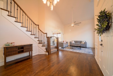 Living area with stairs, high vaulted ceiling, a decorative wall, dark wood floors, and a ceiling fan