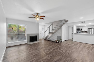 Unfurnished living room featuring a brick fireplace, dark wood finished floors, stairs, and ceiling fan