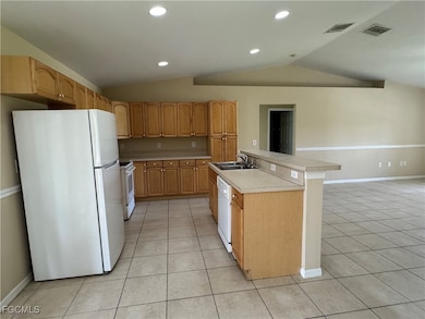 Kitchen with white appliances, vaulted ceiling, light tile patterned floors, light countertops, and recessed lighting
