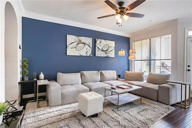 Living area with arched walkways, a ceiling fan, crown molding, and wood finished floors