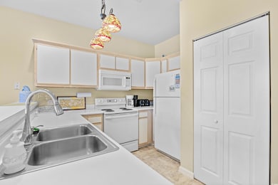 Kitchen with white appliances, light countertops, decorative light fixtures, and white cabinets