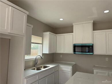 Kitchen featuring stainless steel microwave, a sink, white cabinetry, recessed lighting, and light stone counters