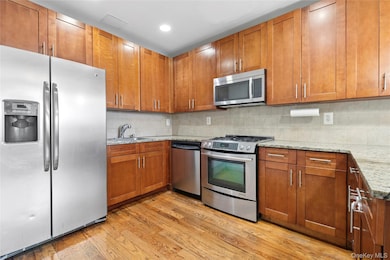 Kitchen with stainless steel appliances, light wood-style flooring, light stone counters, decorative backsplash, and recessed lighting