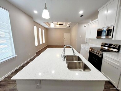 Kitchen featuring appliances with stainless steel finishes, a raised ceiling, a sink, an island with sink, and dark wood-type flooring