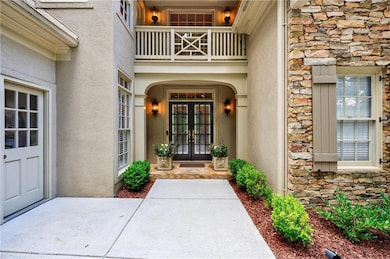 View of exterior entry with french doors, stone siding, stucco siding, and a balcony
