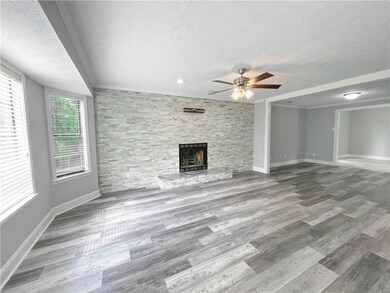 Unfurnished living room featuring a textured ceiling, a ceiling fan, a fireplace, and wood finished floors