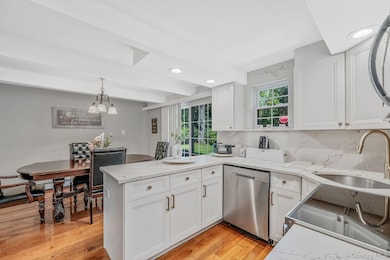 Kitchen with decorative light fixtures, decorative backsplash, a peninsula, stainless steel dishwasher, and white cabinets