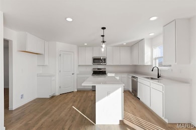 Kitchen with hanging light fixtures, a kitchen island, white cabinetry, stainless steel appliances, and recessed lighting