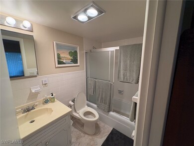Bathroom featuring vanity, combined bath / shower with glass door, tile walls, and wainscoting