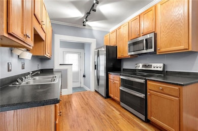 Kitchen with appliances with stainless steel finishes, a sink, track lighting, light wood-type flooring, and crown molding