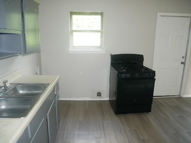 Kitchen featuring gas stove, a sink, wood finished floors, light countertops, and baseboards