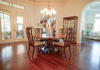 Dining area with french doors, wood finished floors, arched walkways, a chandelier, and ornamental molding