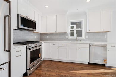 Kitchen with stainless steel appliances, dark wood-style flooring, white cabinets, backsplash, and recessed lighting