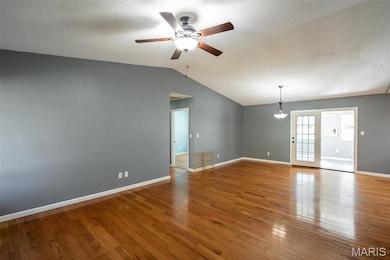 Empty room with wood finished floors, a textured ceiling, vaulted ceiling, and a ceiling fan