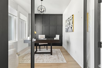 Office with light wood-type flooring, a chandelier, and a decorative wall